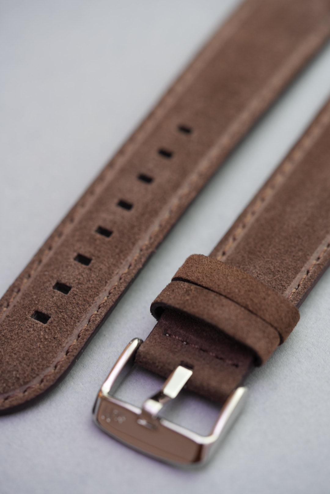 Close-up of brown suede watch strap showing stainless buckle and keeper loops