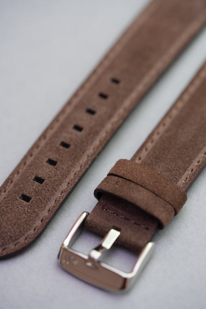 Close-up of brown suede watch strap showing stainless buckle and keeper loops