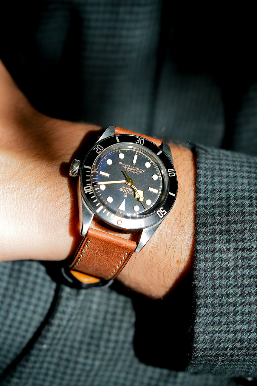Close-up of a wrist wearing a watch with a brown leather strap against a dark background