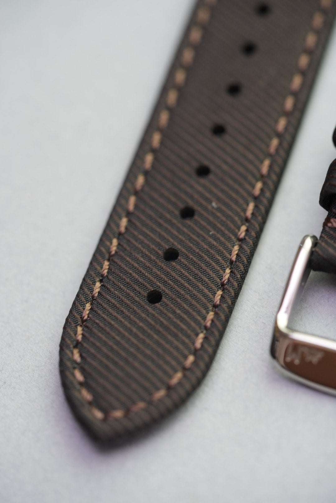 Close-up of recycled gabardine watch strap in clay brown, showing detailed contrast stitching and soft texture.