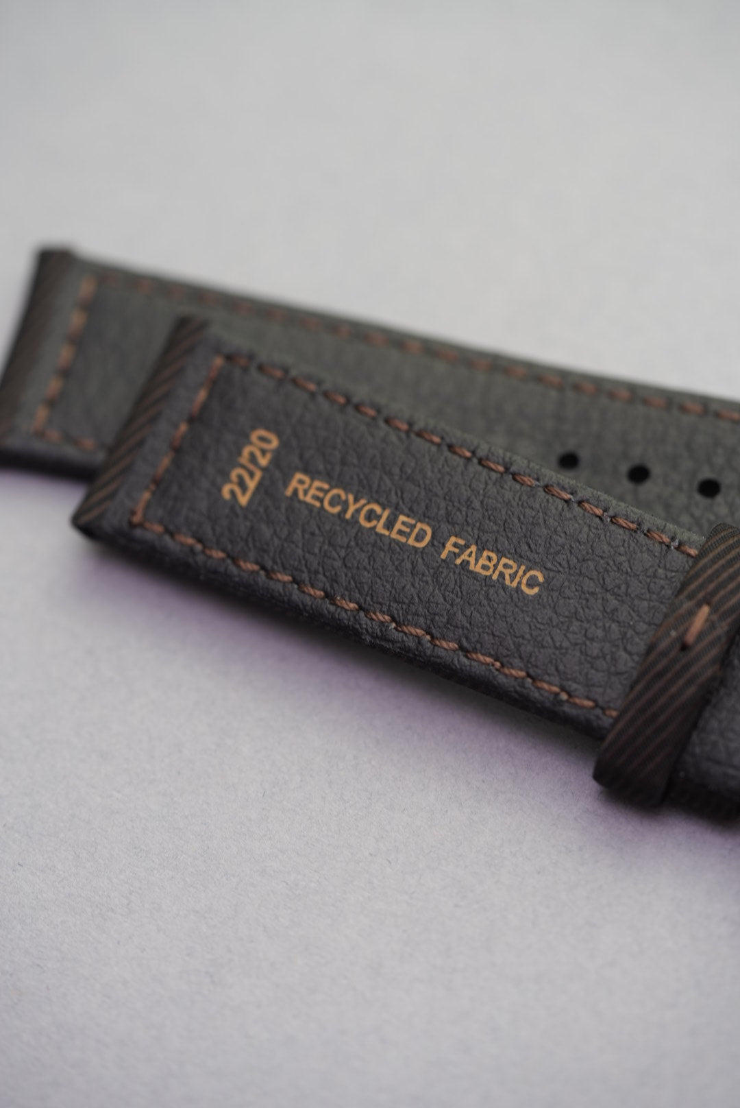Underside stamp showing recycled fabric label and size marking on clay brown strap.