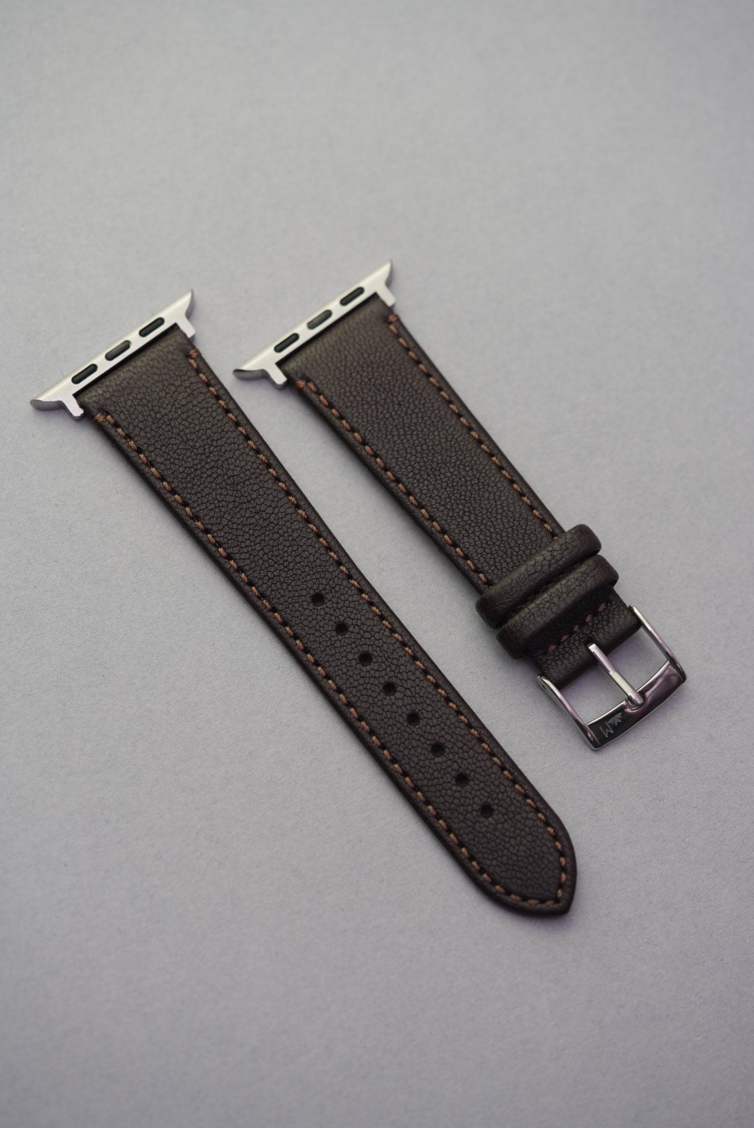 Flat lay of Cortado Chestnut Apple Watch strap showing both sides with stainless steel adaptors and fine-grain finish.
