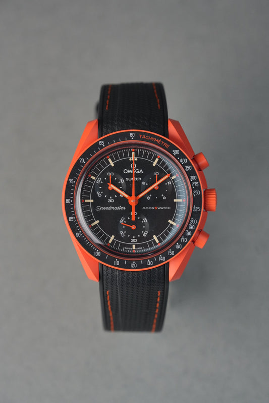 Curved-end black rubber woven MoonSwatch strap with orange contrast stitching and black buckle, designed for a seamless MoonSwatch fit.