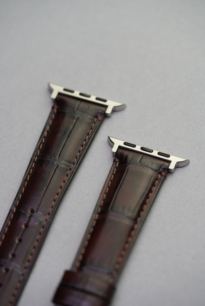 Detail of the stainless steel Apple Watch connectors and textured leather grain on dark brown strap.