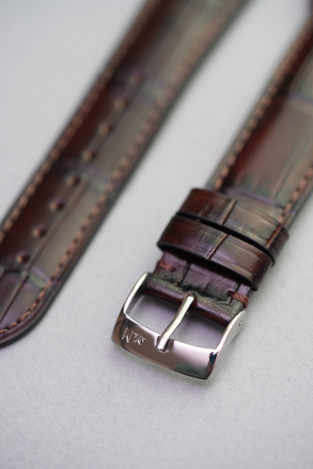 Buckle and loop detail on dark brown Apple Watch strap with embossed calfskin leather finish.