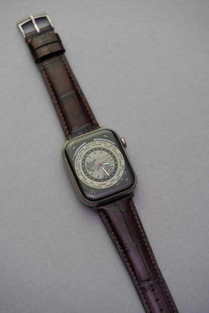 Flat lay of dark brown calfskin Apple Watch strap with alligator texture and polished buckle.