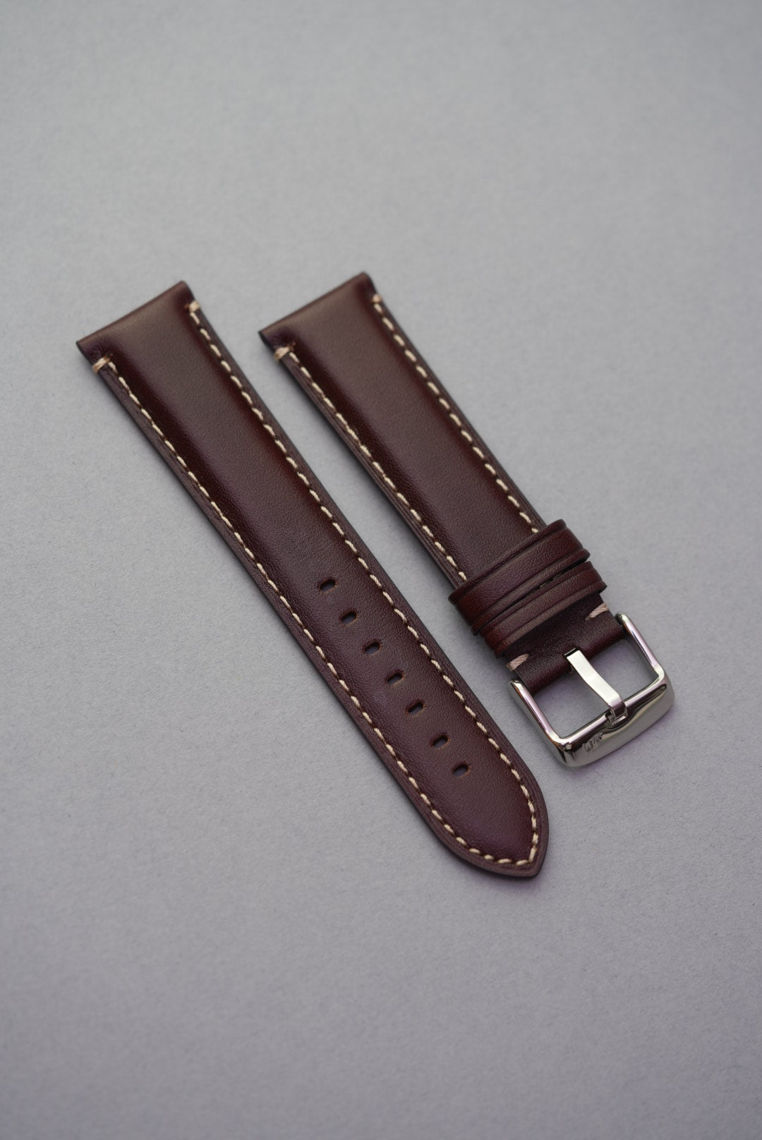 Dark brown leather watch strap with cream stitching laid flat for strap replacement