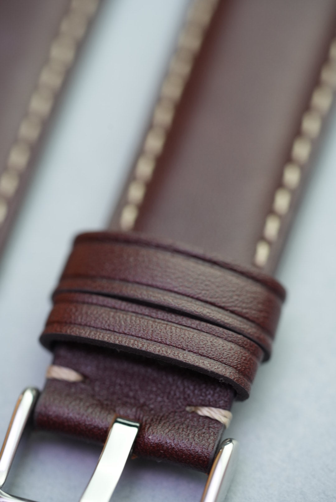Close-up of polished stainless buckle and stitching on dark brown leather strap