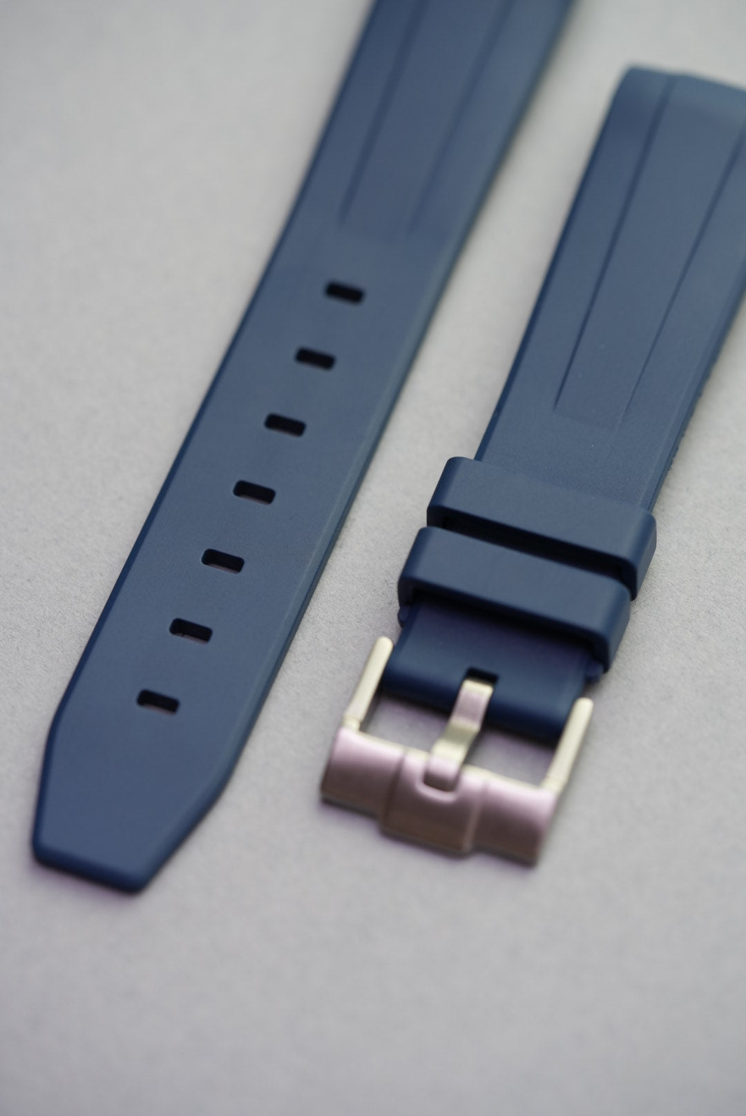 Blue FKM curved rubber strap laid flat with stainless steel buckle, showing adjustment holes and keepers.