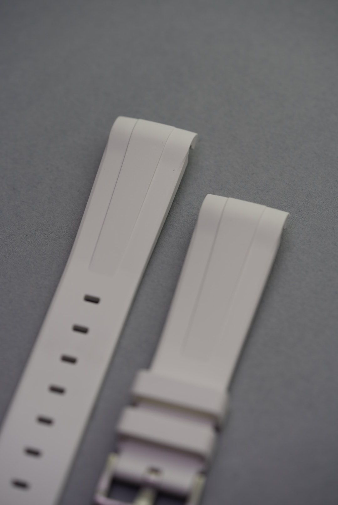 Close-up of unmounted white FKM curved rubber strap on grey background, showing taper and double ridge detailing.