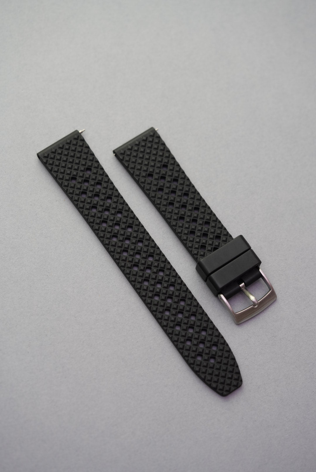  Black FKM rubber honeycomb-pattern watch strap with silver buckle, laid flat on a grey background.