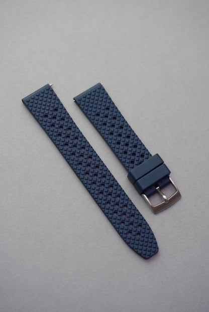 Navy blue FKM rubber honeycomb-pattern watch strap with silver buckle, placed on a neutral grey surface.
