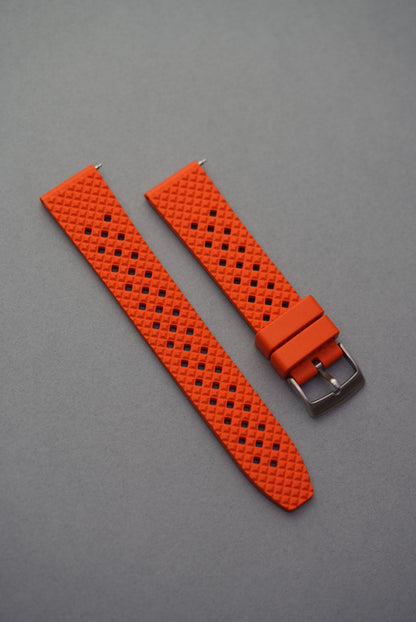 Bright orange FKM rubber honeycomb-pattern watch strap with silver buckle, shown flat on a grey background.
