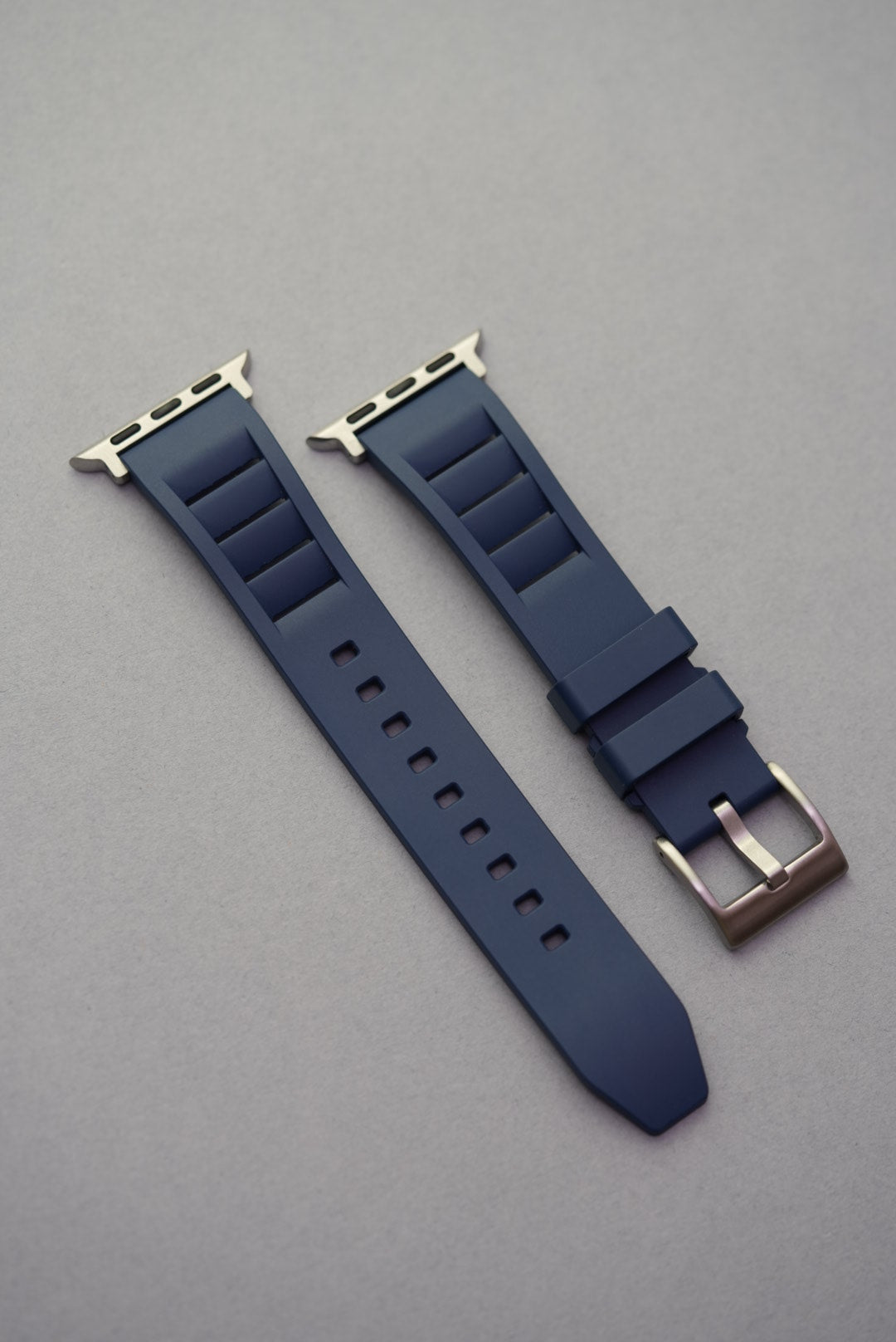 Navy blue FKM rubber strap for Apple Watch, shown flat with stainless steel buckle and integrated adapters.