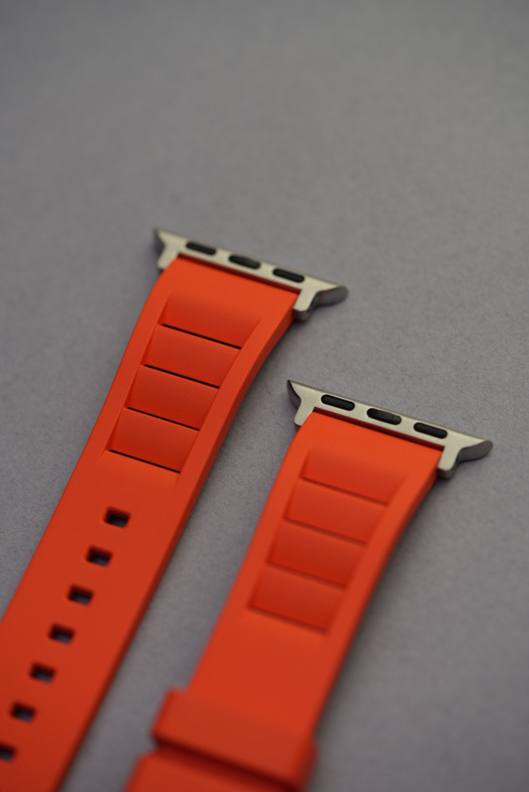 Close-up of Apple Watch connector ends on bright orange FKM rubber strap with vented design.