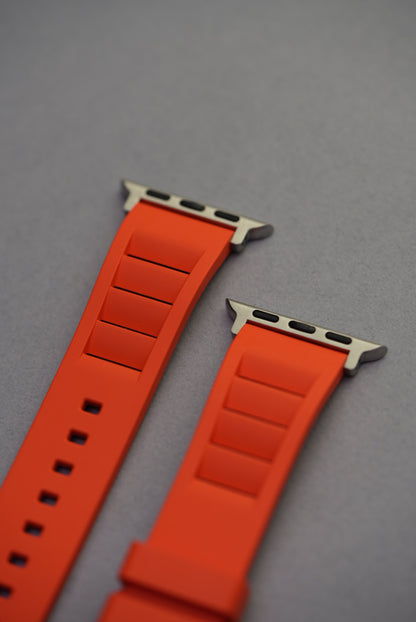 Close-up of Apple Watch connector ends on bright orange FKM rubber strap with vented design.