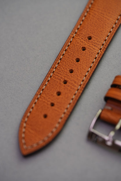 Tapered end of golden brown leather watch strap with stitched edging
