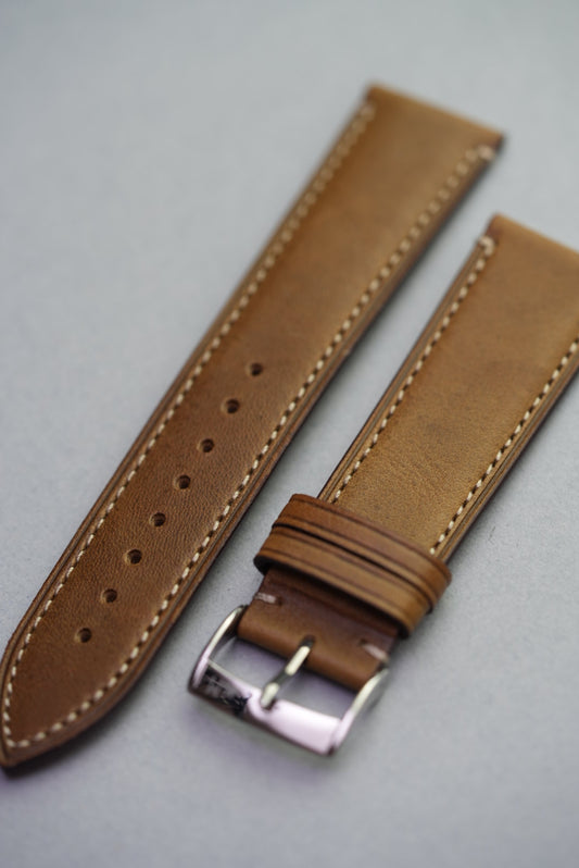 Green calfskin leather watch strap with refined stitching laid flat on neutral background