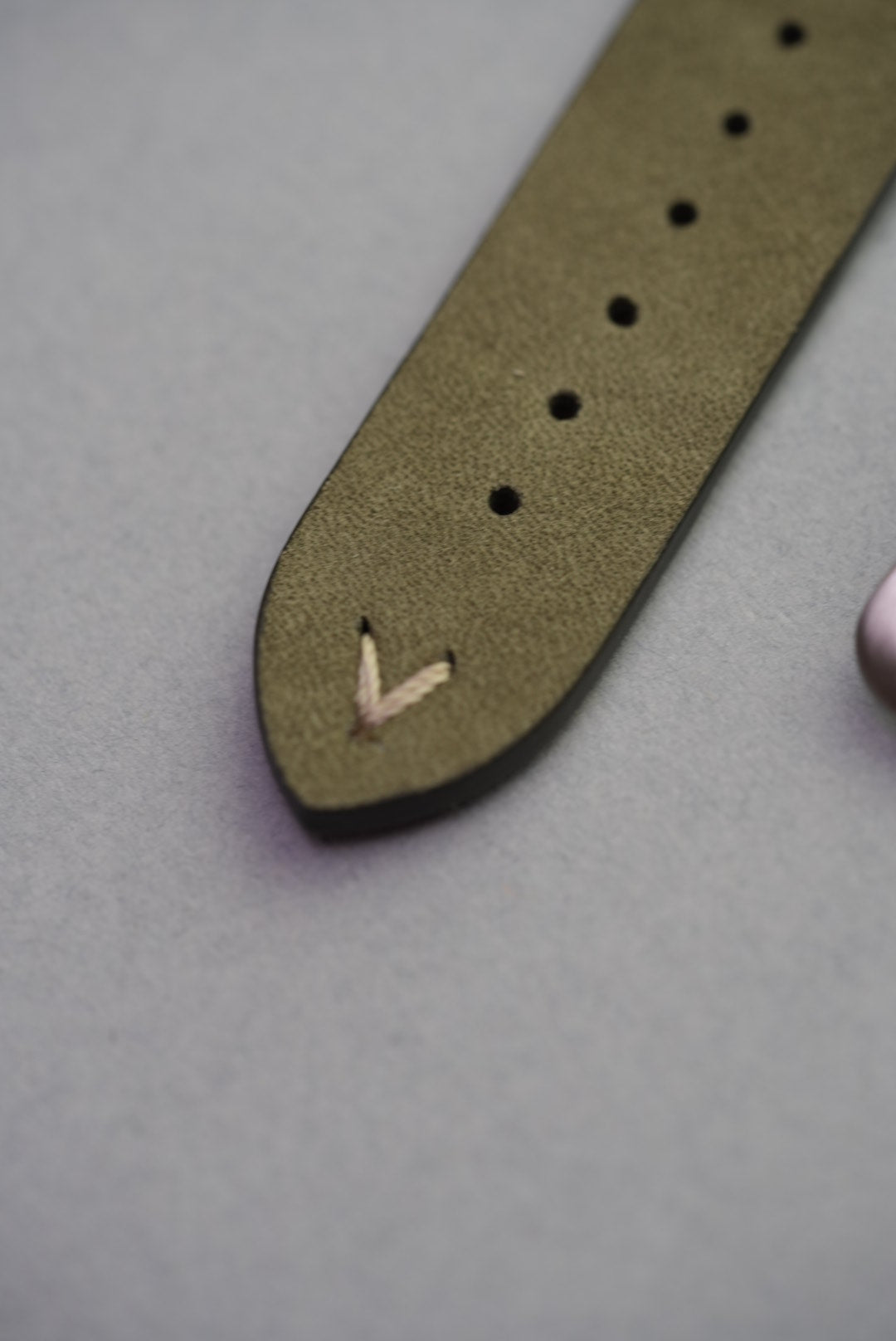 Pointed tip of green Apple Watch strap with decorative lug stitching, calfskin leather finish