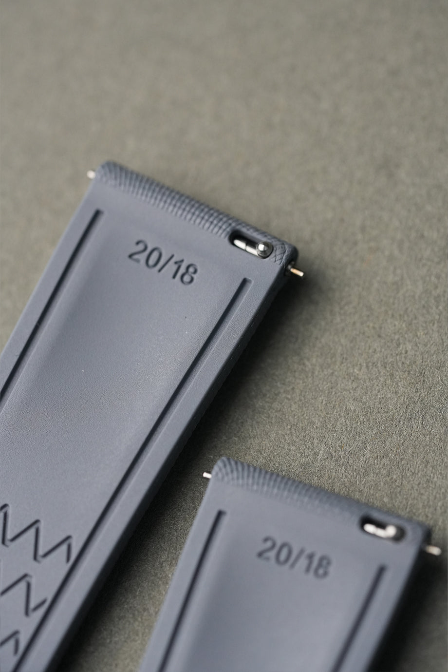 Two gray rectangular objects with '20/18' printed on them, lying on a textured surface.