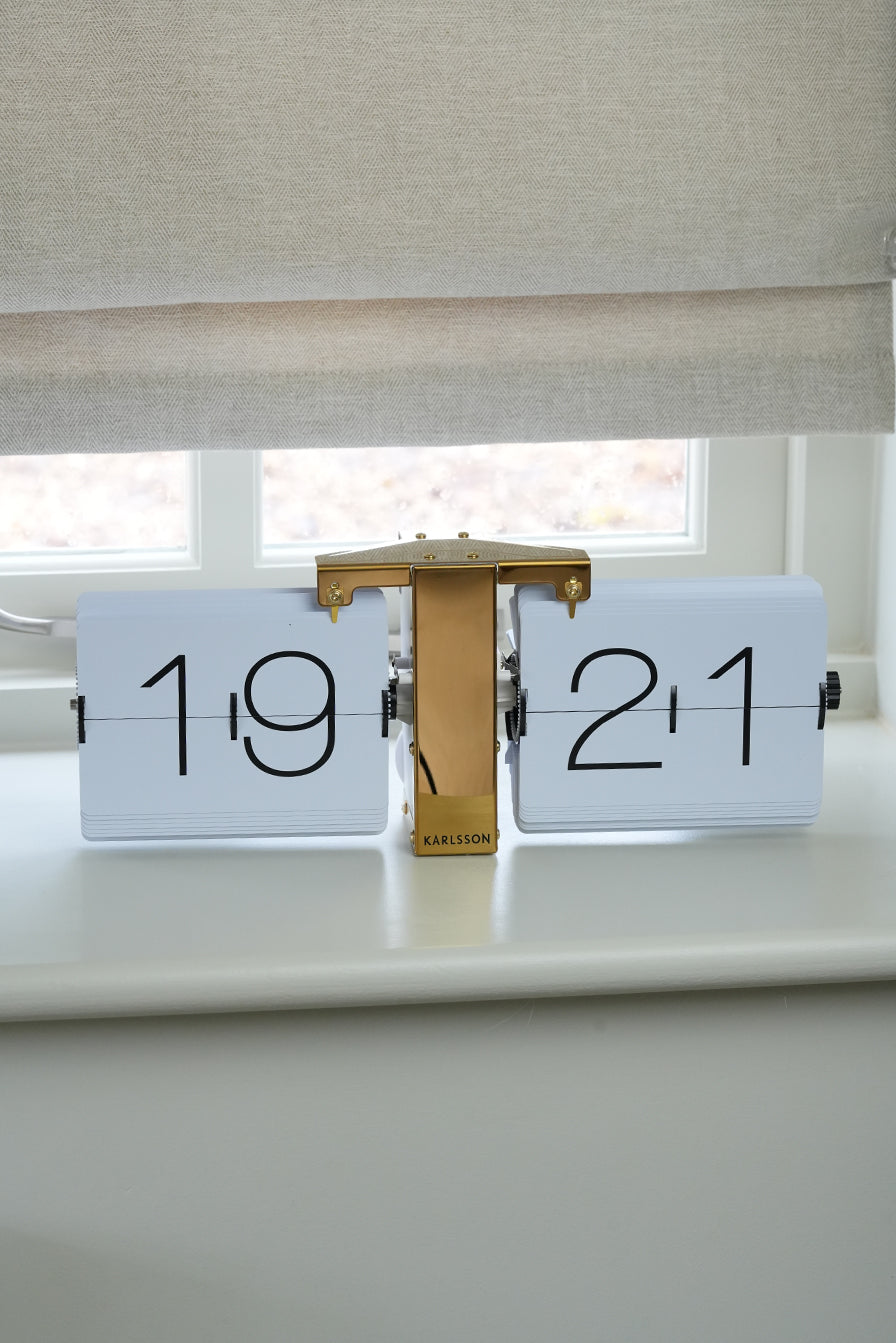 Decorative clock with '1921' on a surface near a window with blinds.