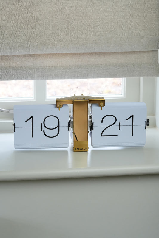Decorative clock with '1921' on a surface near a window with blinds.