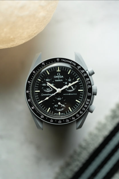 Close-up of a black and silver watch on a light surface.