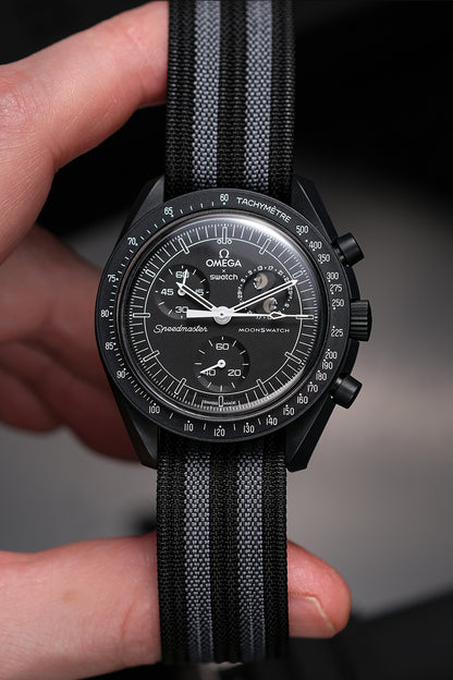 MoonSwatch nylon deployant strap in black and grey — fitted on Snoopy New Moon MoonSwatch, held in hand