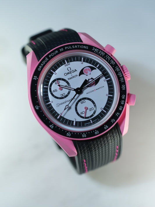 Angled studio shot of the Swatch MoonSwatch Pink Moonphase on black strap with pink stitching – pulsometer bezel in focus.