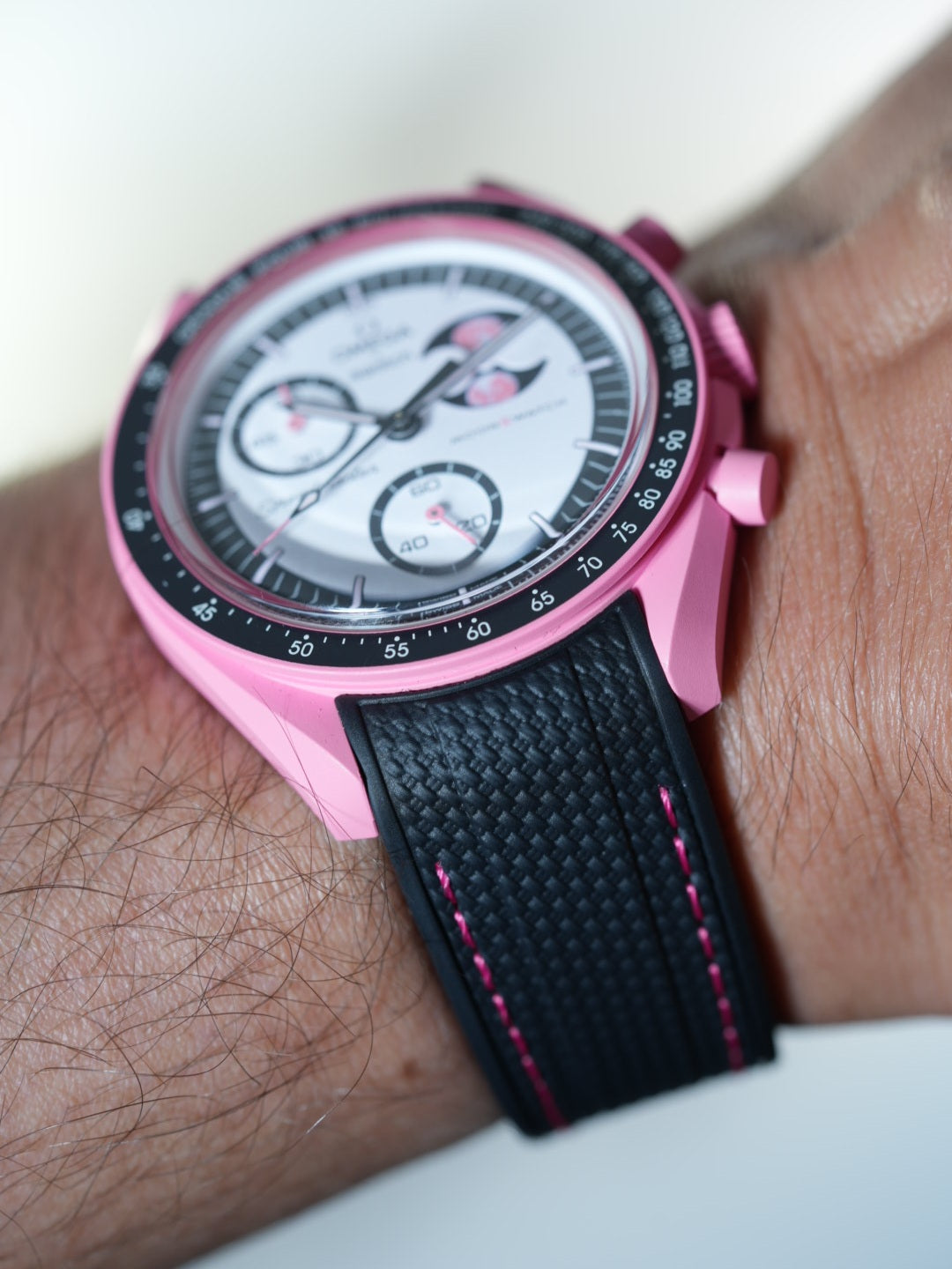 Angled studio shot of the Swatch MoonSwatch Pink Moonphase on black strap with pink stitching – pulsometer bezel in focus.