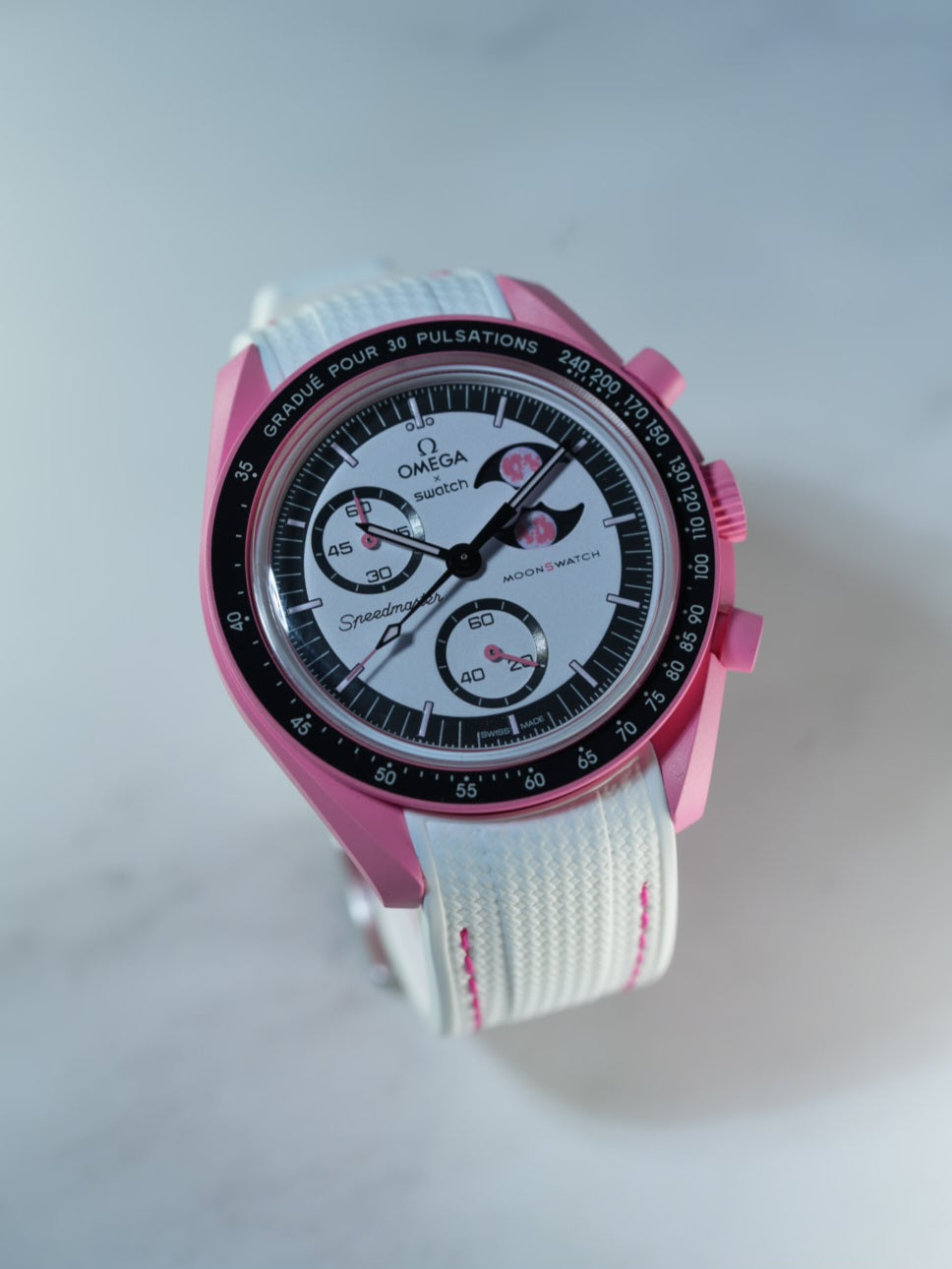 Angled studio shot of the MoonSwatch Pink Moonphase paired with a crisp white strap and pink detail stitching.