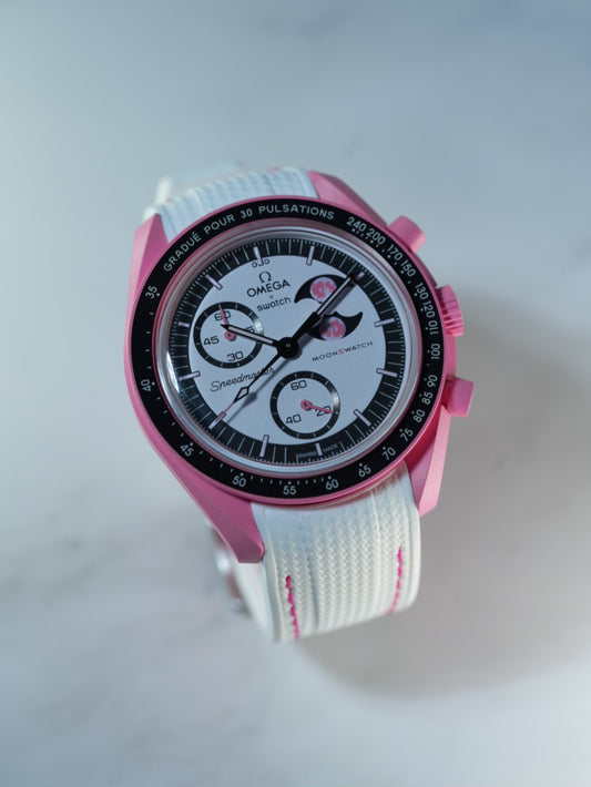 Angled studio shot of the MoonSwatch Pink Moonphase paired with a crisp white strap and pink detail stitching.