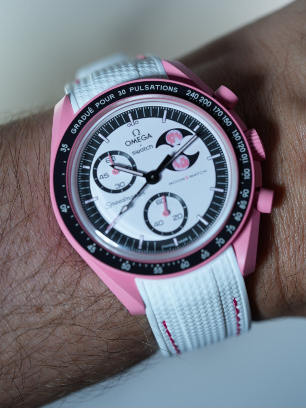 MoonSwatch Pink Moonphase on wrist with white strap and pink stitch – bold contrast with soft springtime tones.