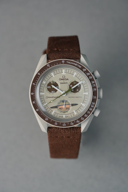 Brown suede strap on MoonSwatch Saturn — front view showing brushed suede texture against warm beige case