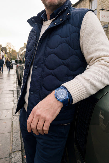 Man wearing a navy puffer vest and blue watch, standing on a street.