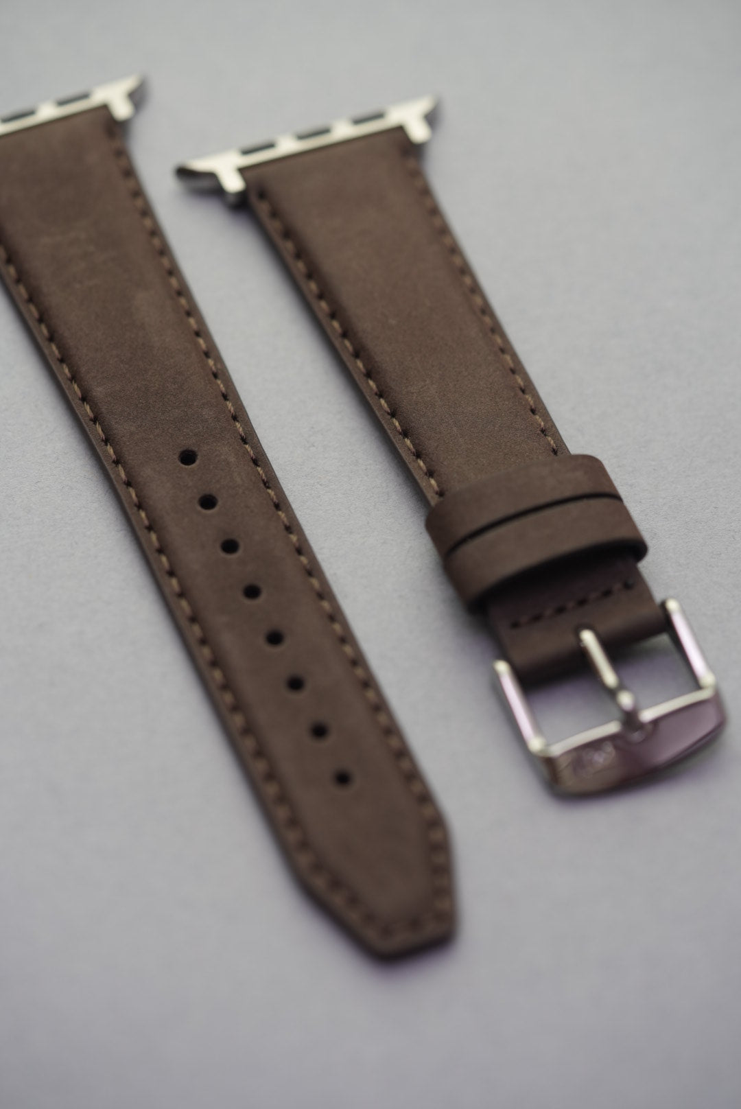 Detailed view of the brown Apple Watch strap adapters and curved leather finish.