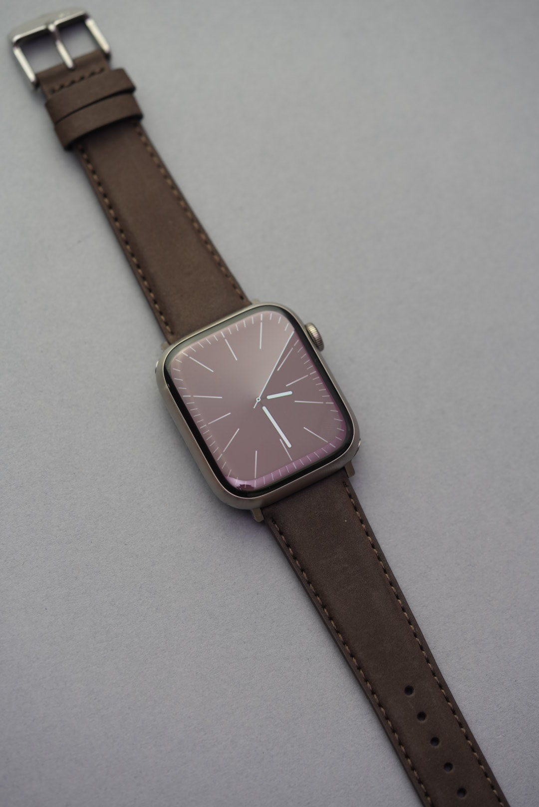 Apple Watch fitted with a brown nubuck strap, photographed from top-down showing full strap length.