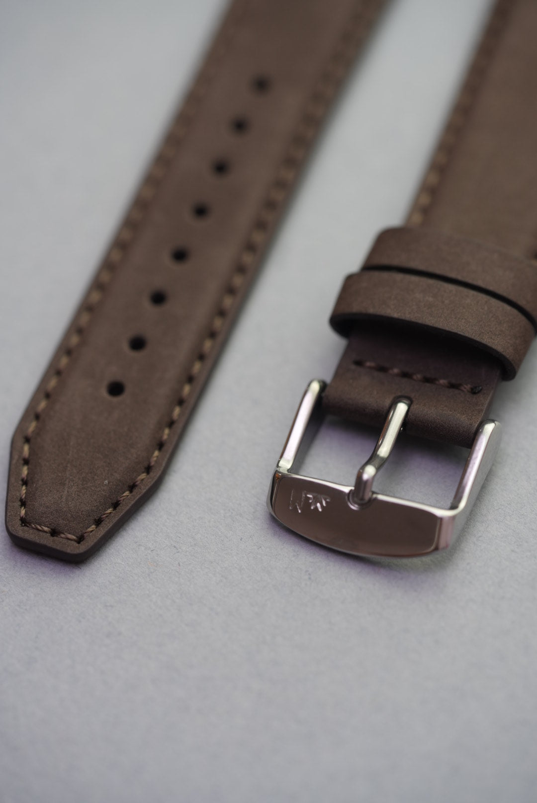 Close-up of brown nubuck leather strap for Apple Watch with polished buckle and stitched detailing.