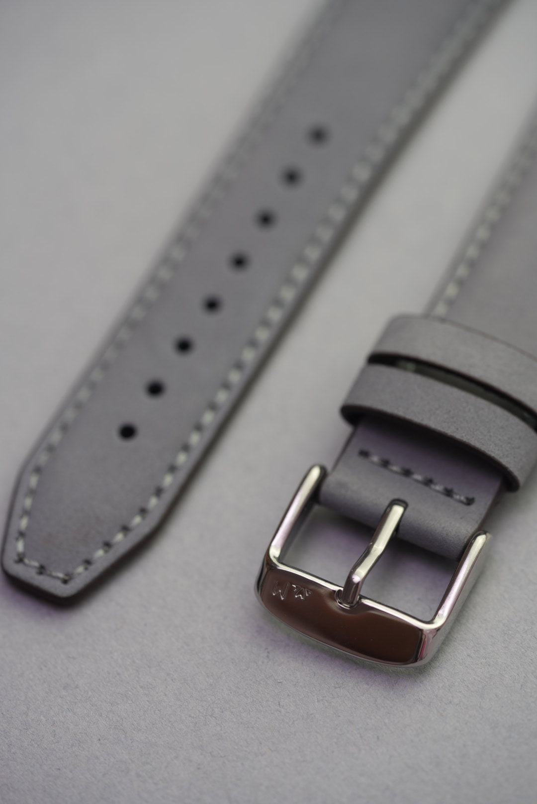 Detail view of the grey nubuck Apple Watch strap's buckle and keeper loops, with engraved branding.