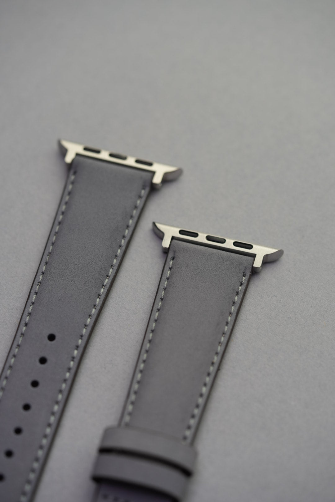 Close-up of grey nubuck strap with Apple Watch adapters, showing soft leather texture and stitching detail.
