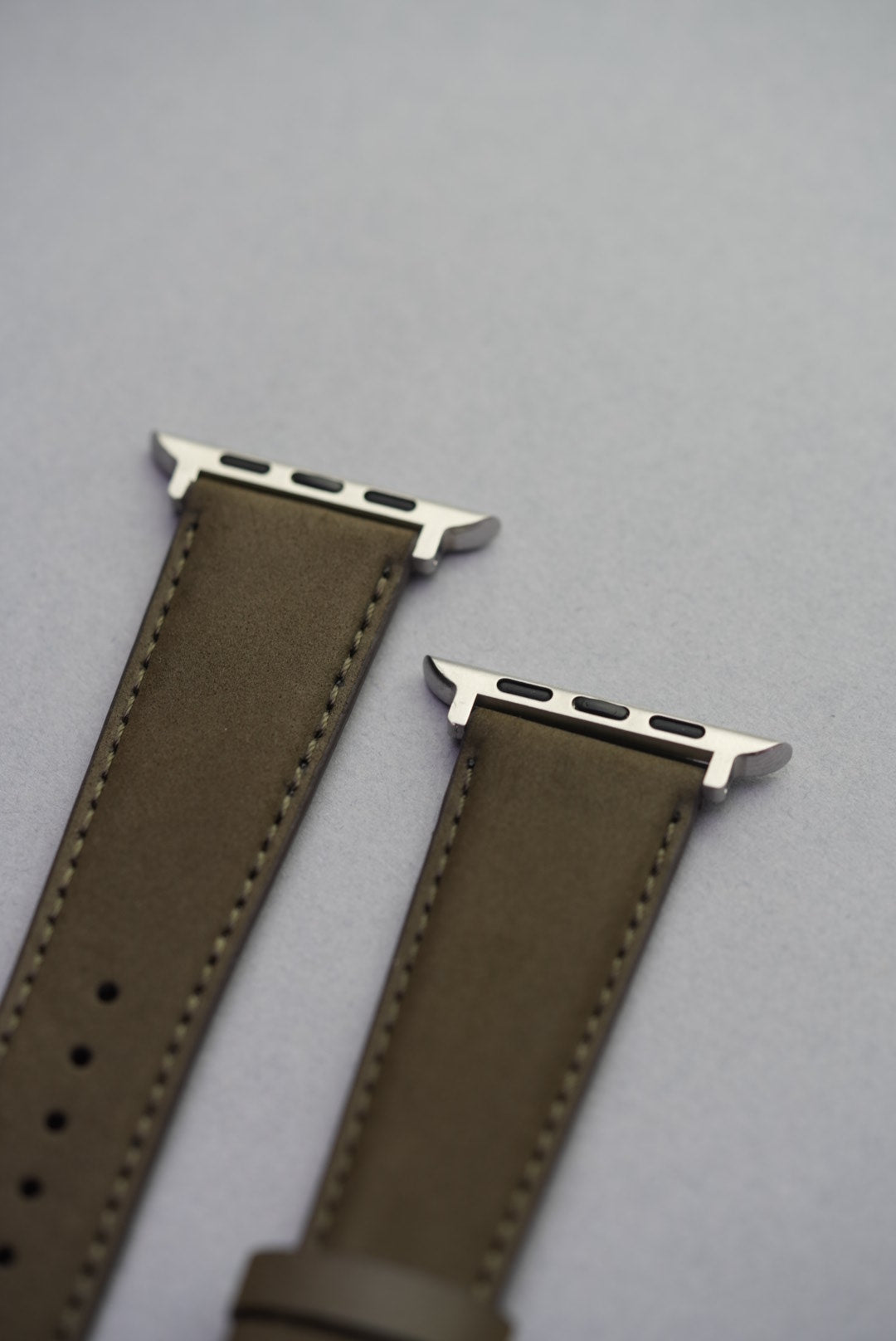 Olive nubuck leather Apple Watch strap with adapters, laid flat to show full strap profile.
