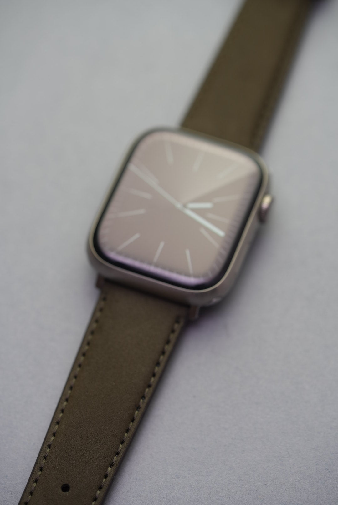 Close-up of olive nubuck strap for Apple Watch with contrast stitching and fine leather grain.