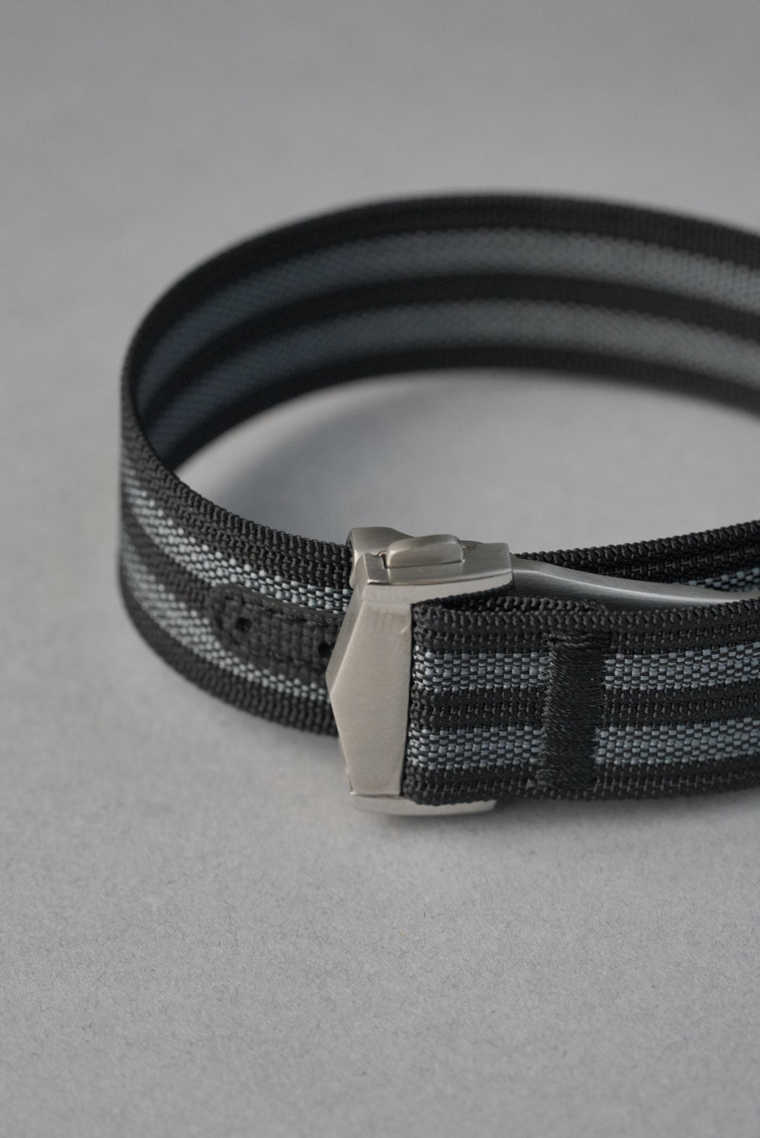 Black woven belt with a silver buckle on a gray background
