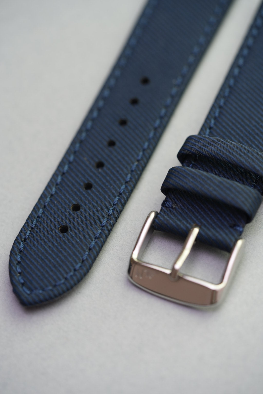 Detail view of the Ocean Blue recycled strap showing curved tip, punch holes, and stitched fabric grain.