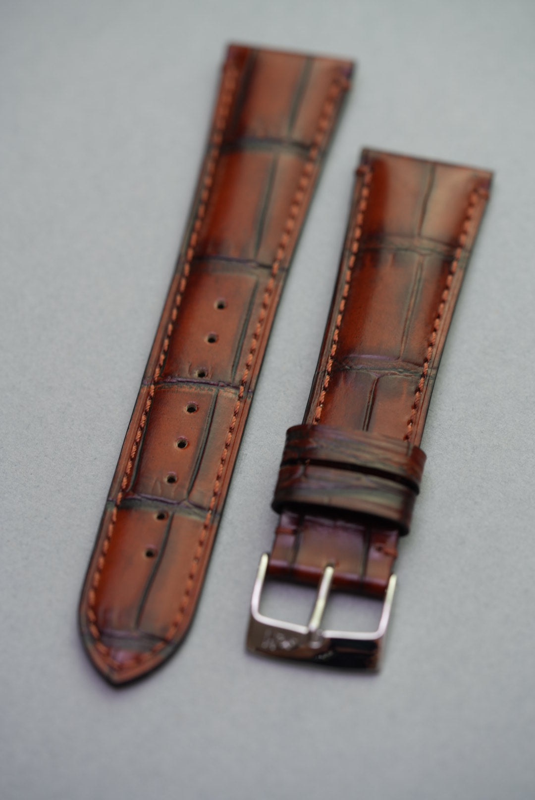 Brown leather watch strap with silver buckle on a gray background