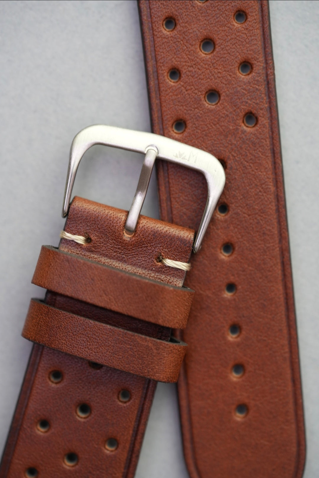 Perforated brown leather watch strap laid flat with replacement buckle