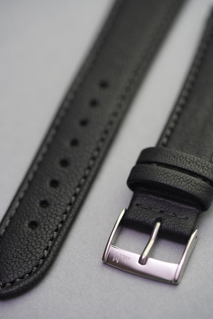 Close-up of Piano Noir strap buckle and double leather keepers, crafted in deep matte black sheepskin.