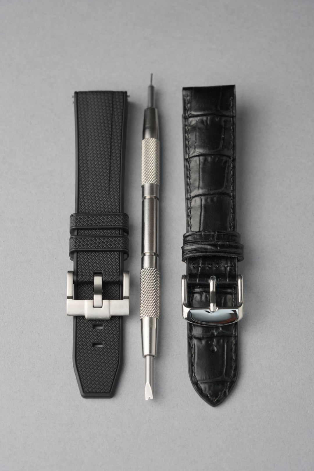 Two black watch straps with silver buckles on a gray background