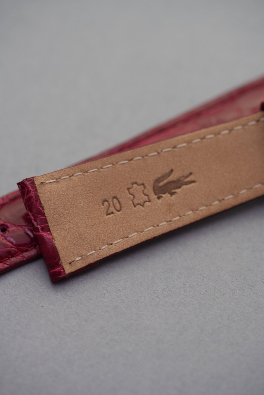 Underside of ruby red crocodile leather watch strap showing 20mm width marking and natural calfskin lining.