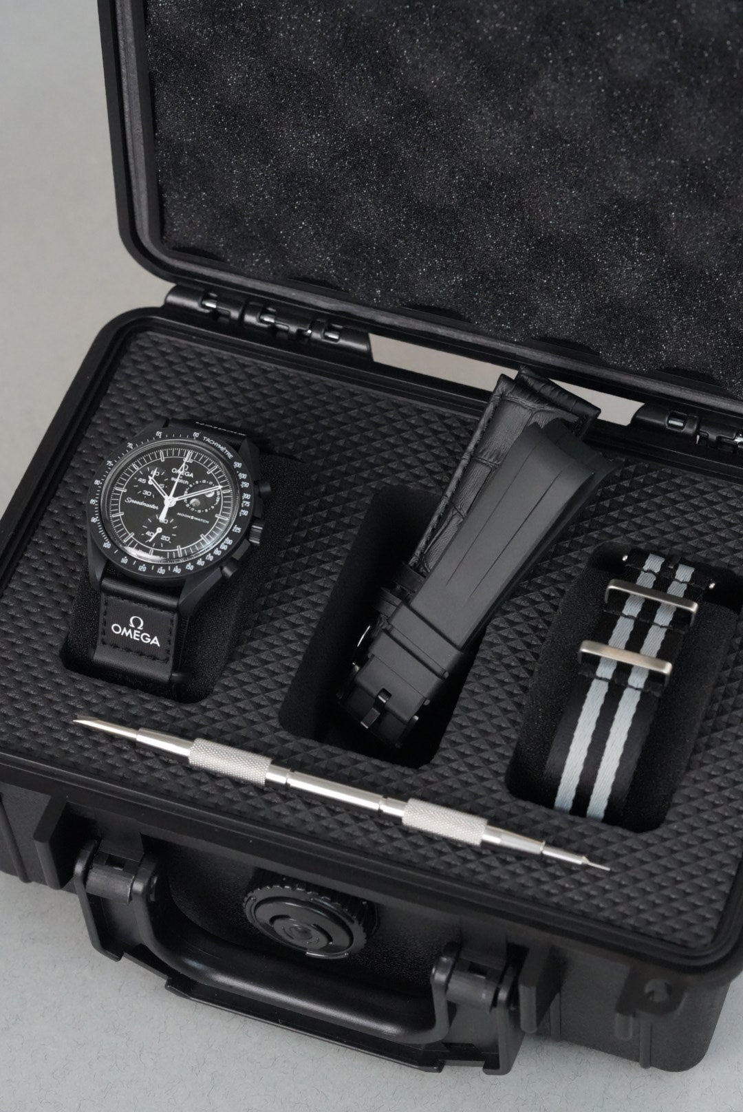 Black watch, straps and tools in a black case on a light grey background